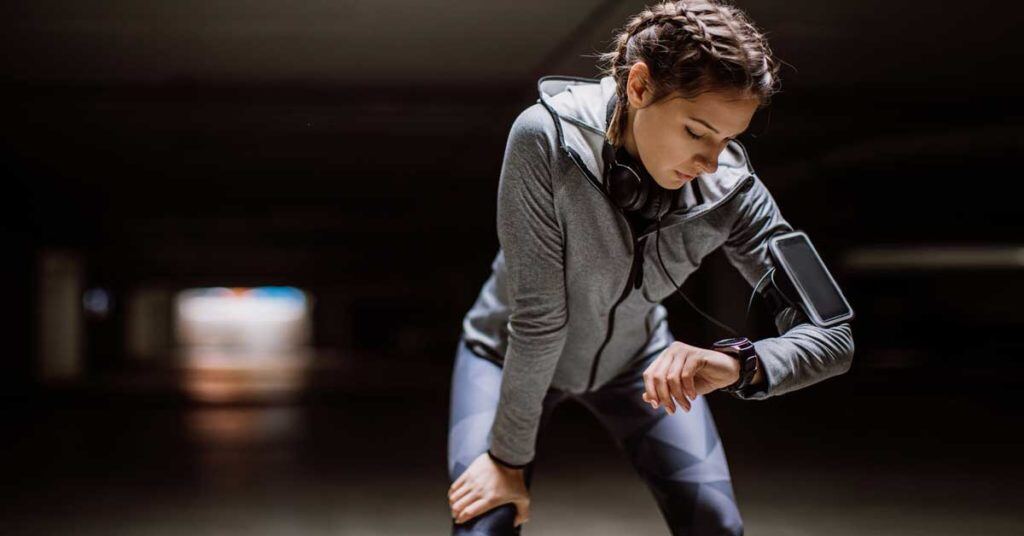 Female athlete wearing sportswear and headphones, checking her wrist-worn wearable device, symbolizing the integration of technology in fitness and sports.